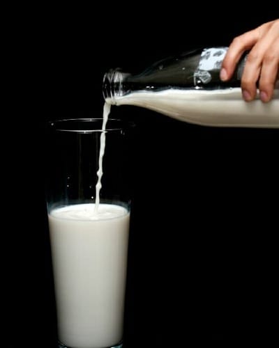 person pouring milk on clear drinking glass
